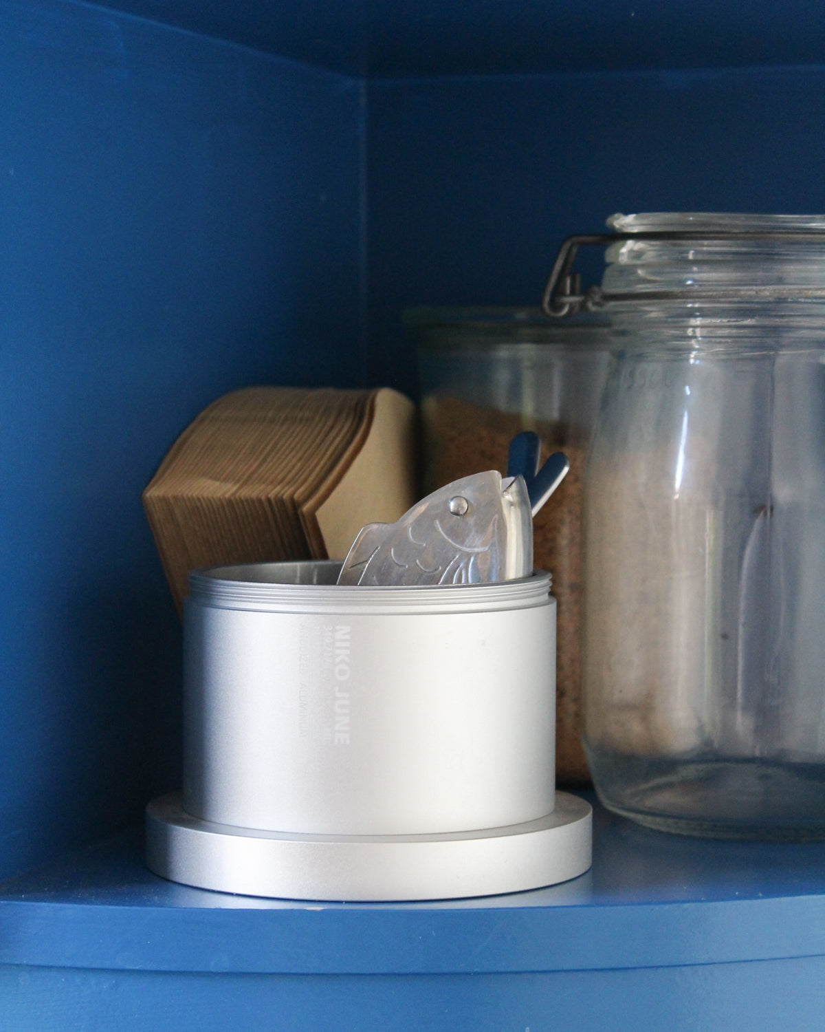 Chamber Series Grey aluminium storage container by NIKO JUNE displayed on a blue shelf alongside glass jars and small everyday objects.