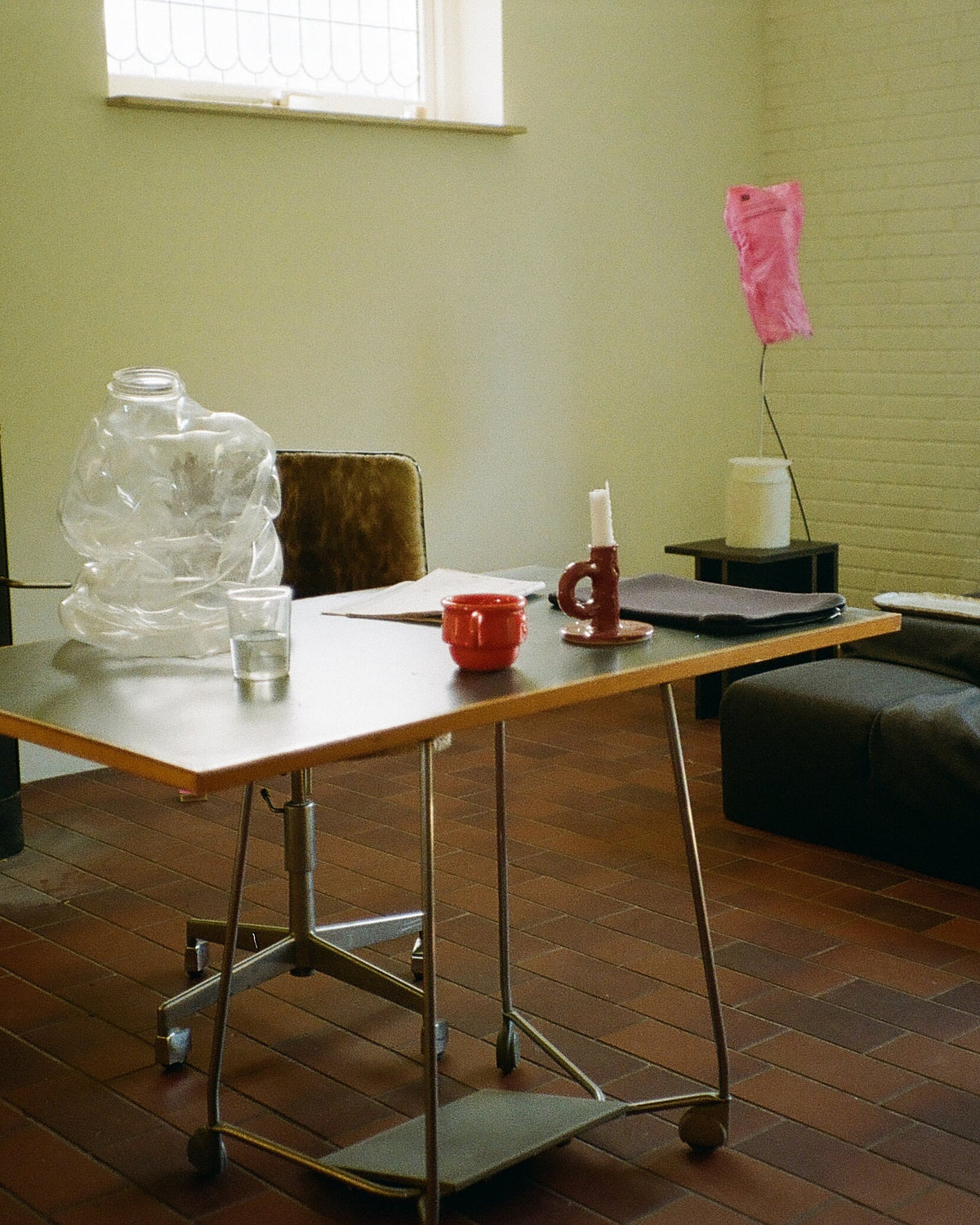 Studio Candlestick Burgundy by NIKO JUNE displayed on a wooden table in a bright interior with pale green walls and other decorative objects.