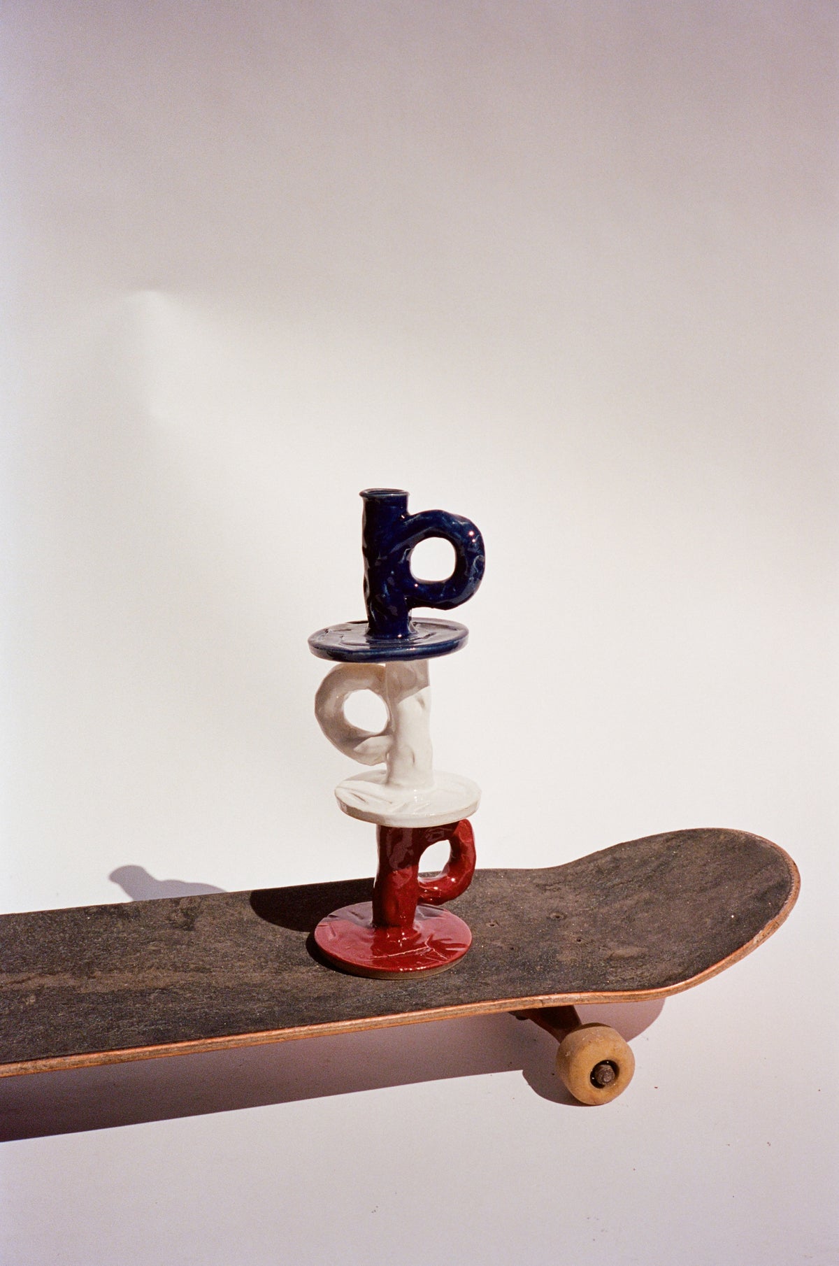 Studio Candlestick Burgundy, White and Dark Blue by NIKO JUNE displayed on a Skateboard highlighting its sculptural ceramic form.