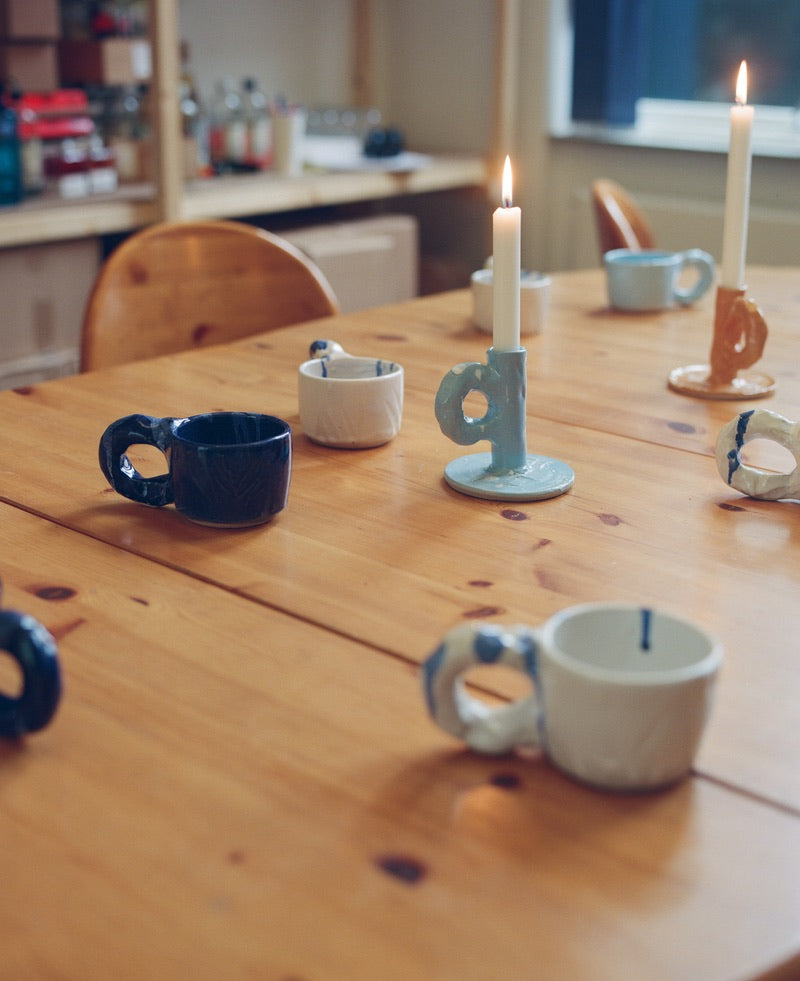 Studio Series ceramic cups by NIKO JUNE in different colours arranged on a wooden dinner table.