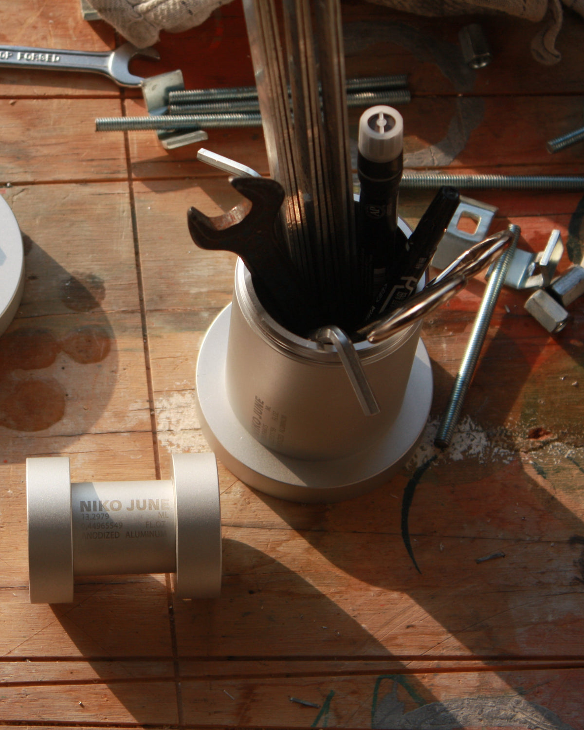 Close-up of a Chamber Series aluminium containers by NIKO JUNE on a wooden tabletop, surrounded by tools and everyday objects in warm natural light.