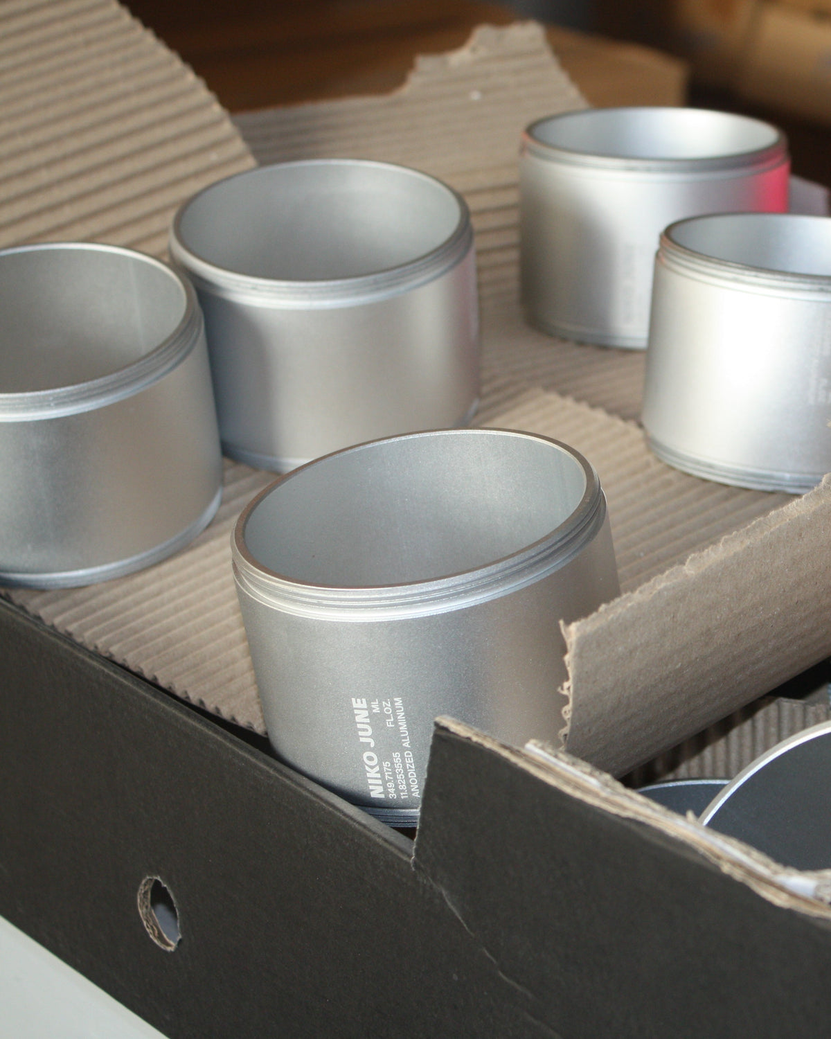Several silver-grey Chamber Series aluminium containers by NIKO JUNE arranged together in a workshop in the assemble process, showing their cylindrical shapes and anodized finishes.