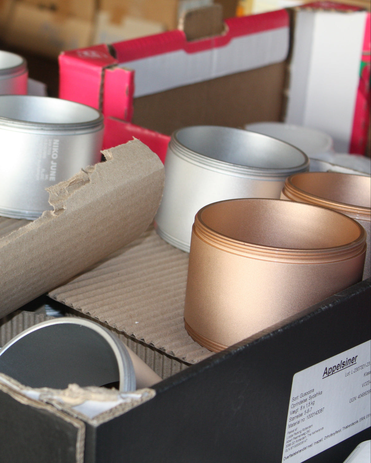 Chamber Series aluminium storage containers by NIKO JUNE in Grey and Gold arranged together in a workshop during assembly, showing the different anodized finishes and cylindrical forms.