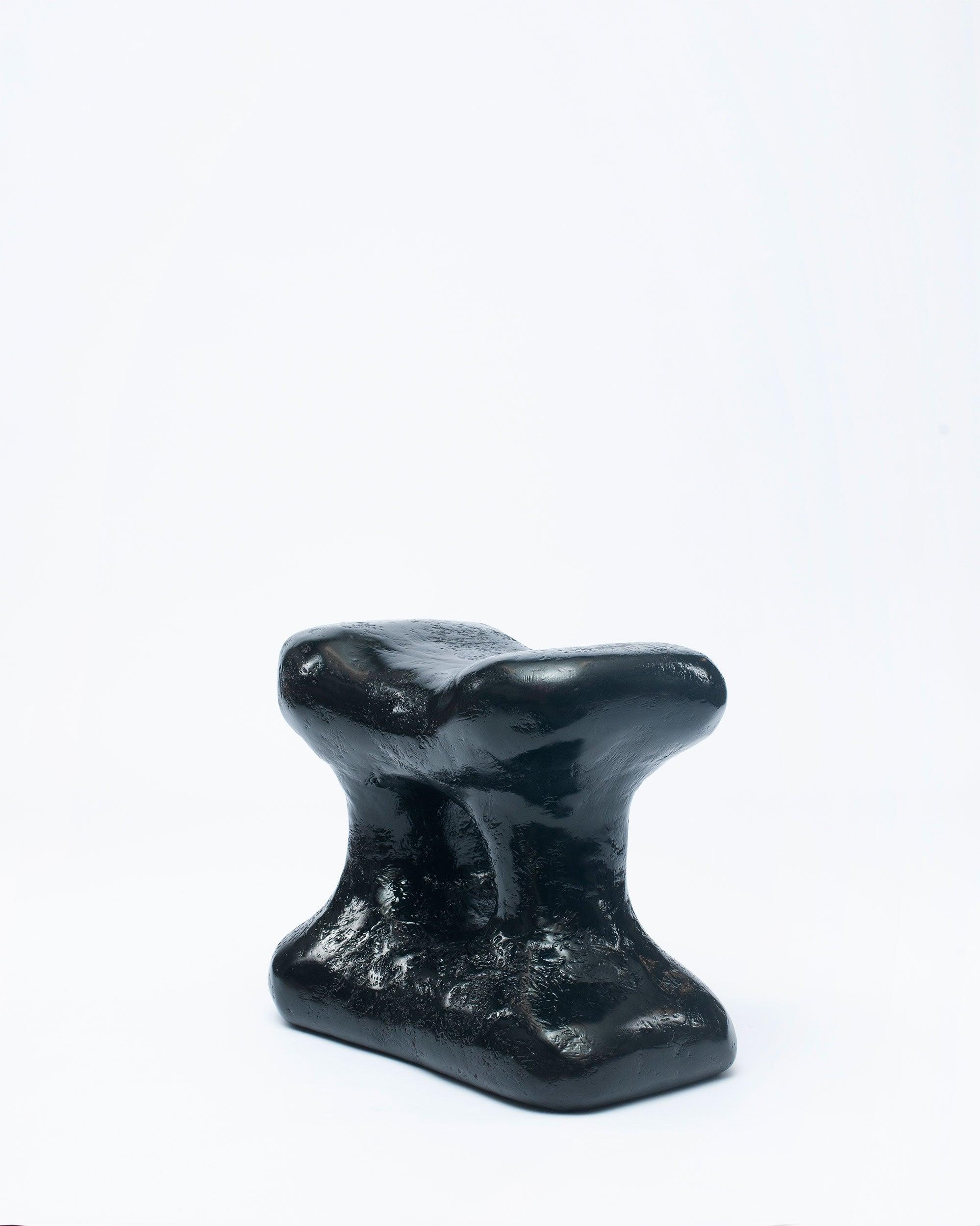 Hand-carved collectible black stool by NIKO JUNE in white background leaning to the right