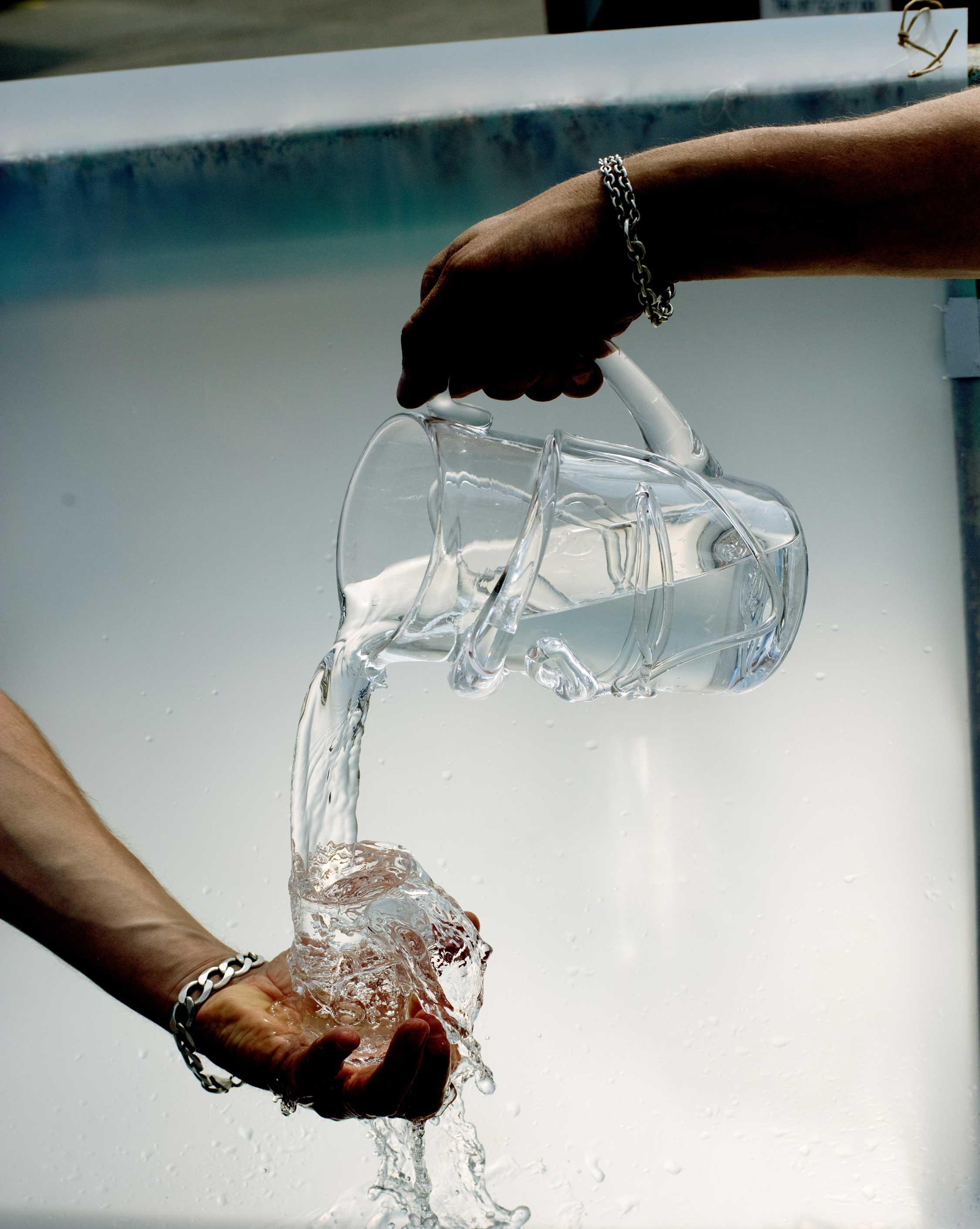 Hands holding a designer glass pitcher with melted glass details on white background