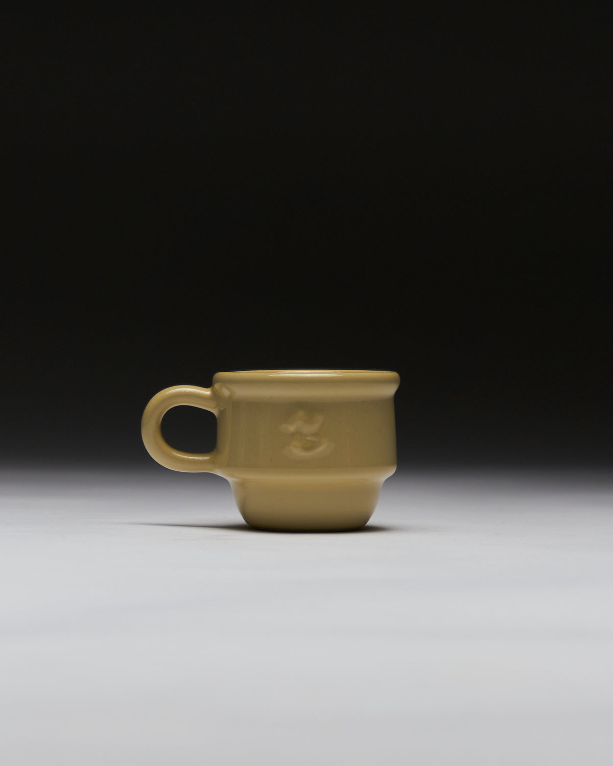 Beige Kantine ceramic espresso cup by NIKO JUNE, made from glossy stoneware with a rounded handle and embossed logo.